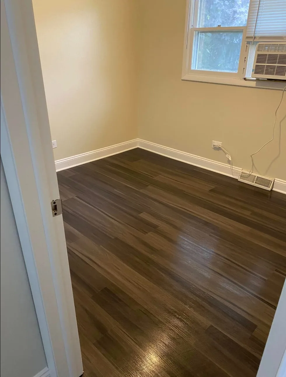 Finished bedroom with dark wood-look LVP flooring, freshly painted cream walls and white baseboards and door trim