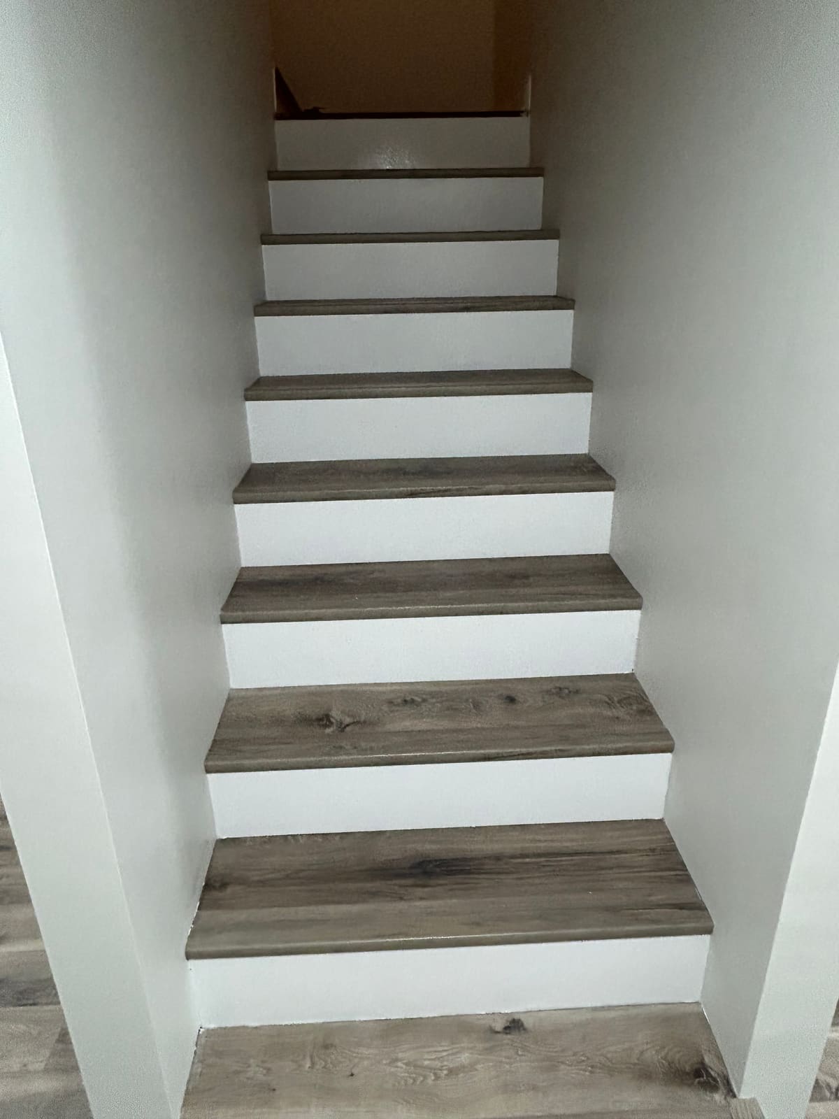 Staircase finished with gray-brown wood-look plank treads and freshly painted white risers and side walls, with matching plank flooring at the base of the run