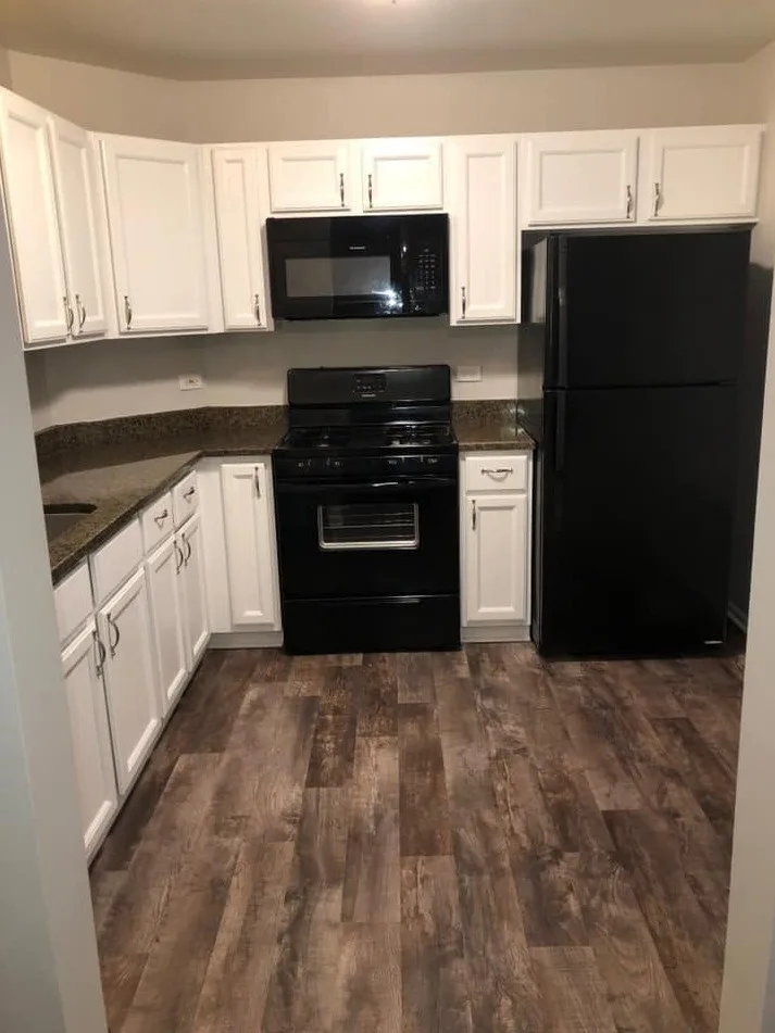 Remodeled kitchen with white raised-panel cabinets, speckled granite countertops, a black range, microwave and refrigerator, and gray wood-look plank flooring