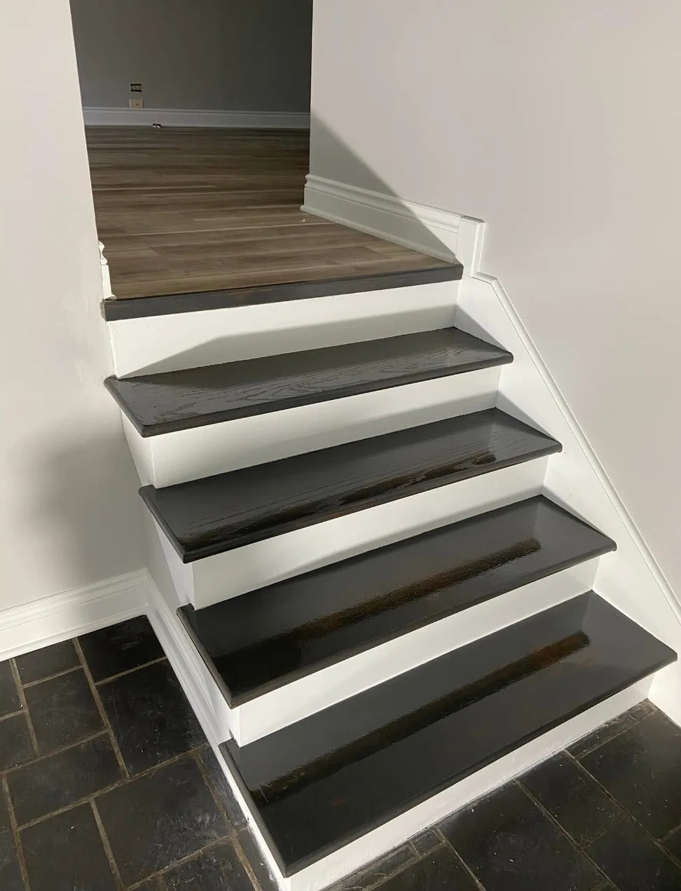 Refinished staircase with dark-stained wood treads, freshly painted white risers and trim, a wood-look landing and dark tile at the base