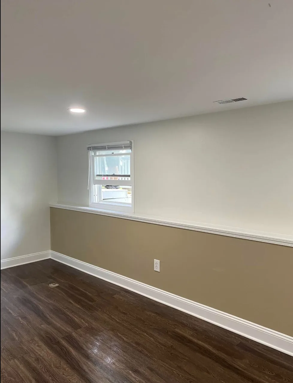 Finished room with two-tone painted walls — soft white above a white chair rail and tan below — white baseboards and window trim, and dark wood-look LVP flooring